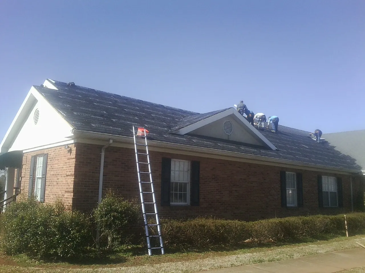 Crew tearing shingles off a brick ranch roof with a ladder set — Emergency Roof Repair work by our crew in Nephi