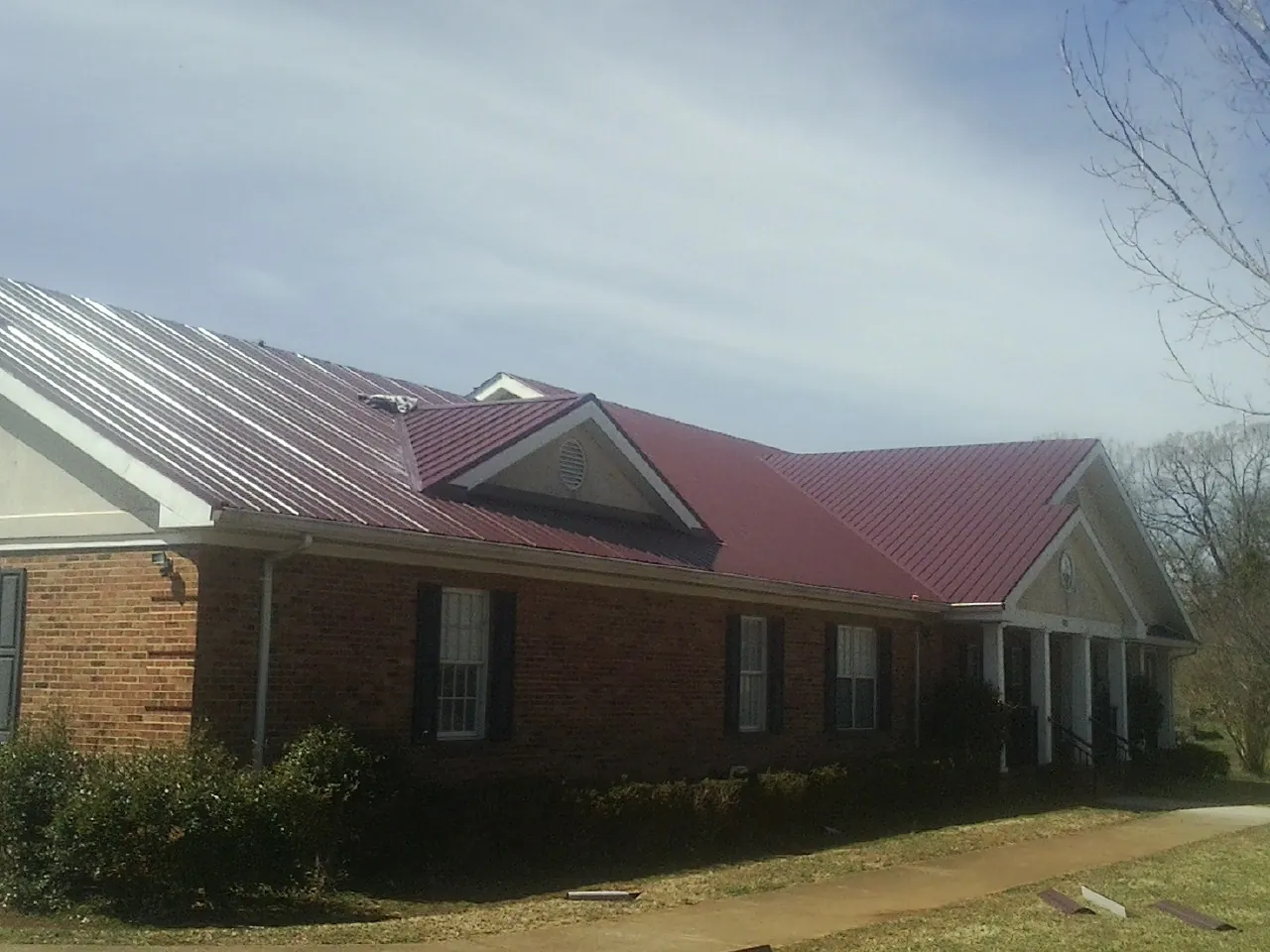 Red metal roof with gabled entries on a long brick building, from a Hail Damage Roof Repair job in Nephi