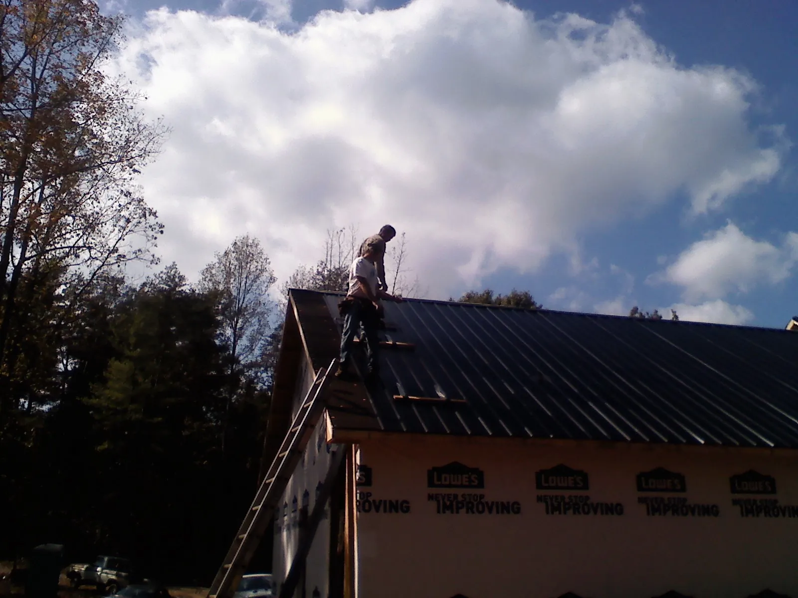 Roofer fastening dark metal panels high against a cloudy sky, from a Roof Inspection job in Nephi