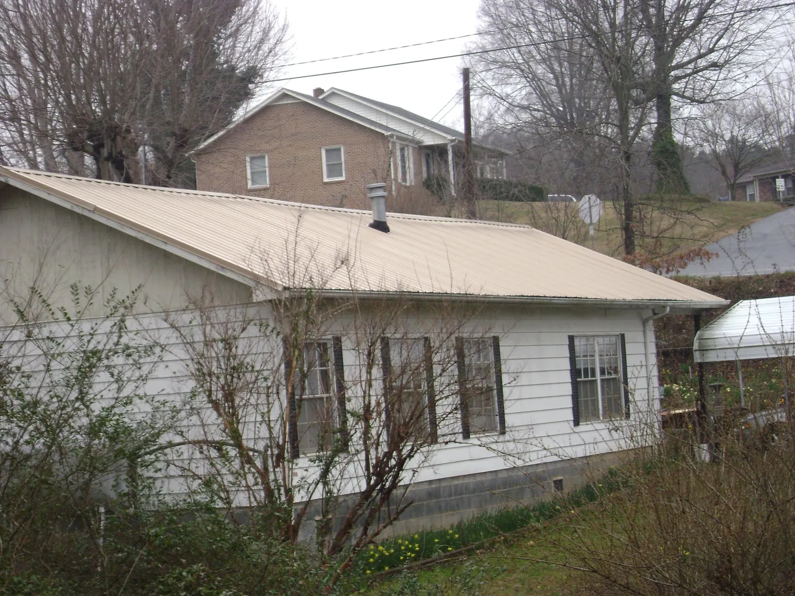 Tan metal roof on a white sided house set into a hillside — Commercial Roofing by Roofing Brothers in Nephi