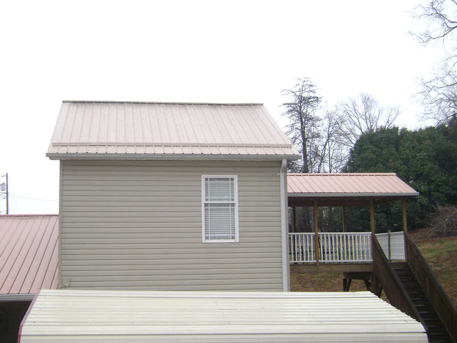 Tan metal roofs on a two story addition and attached porch, from a Roof Replacement job in Nephi